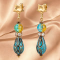 Heartfelt Creations artisan drop earrings with gold star studs, marbled blue-yellow beads, and teal teardrop charms.