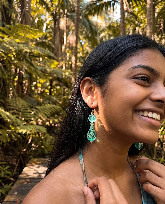 Heartfelt Creations artisan teardrop dangle earrings in teal and lime green glass worn by a smiling woman in a forest