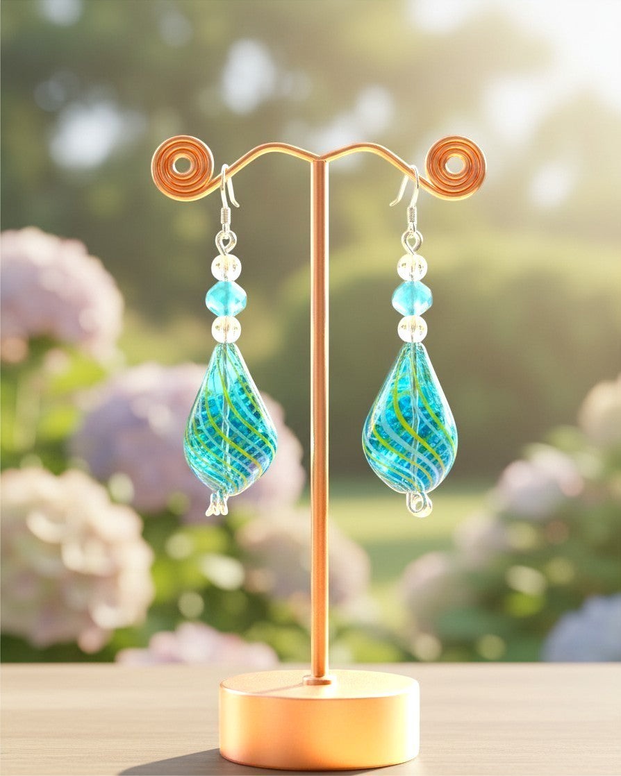 Heartfelt Creations handcrafted teal and lime-green glass teardrop dangle earrings with faceted bead accents on a stand.