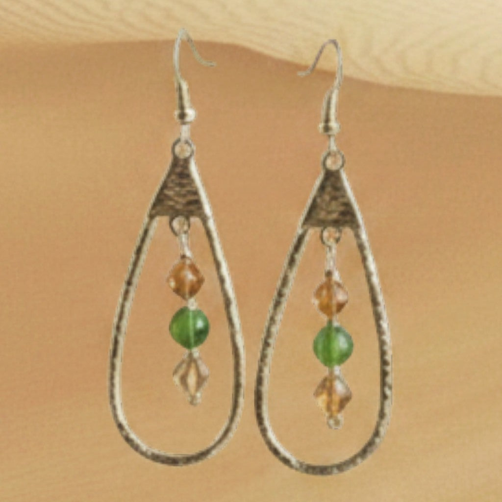 Heartfelt Creations teardrop earrings with amber and green beads hanging against a soft beige fabric background.