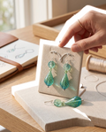 Heartfelt Creations artisan teardrop glass earrings in teal and lime green with floral beads on a display stand.
