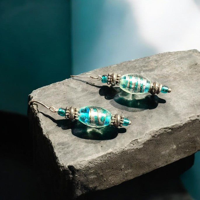 Heartfelt Creations artisan turquoise glass dangle earrings with metallic accents on a dark stone surface