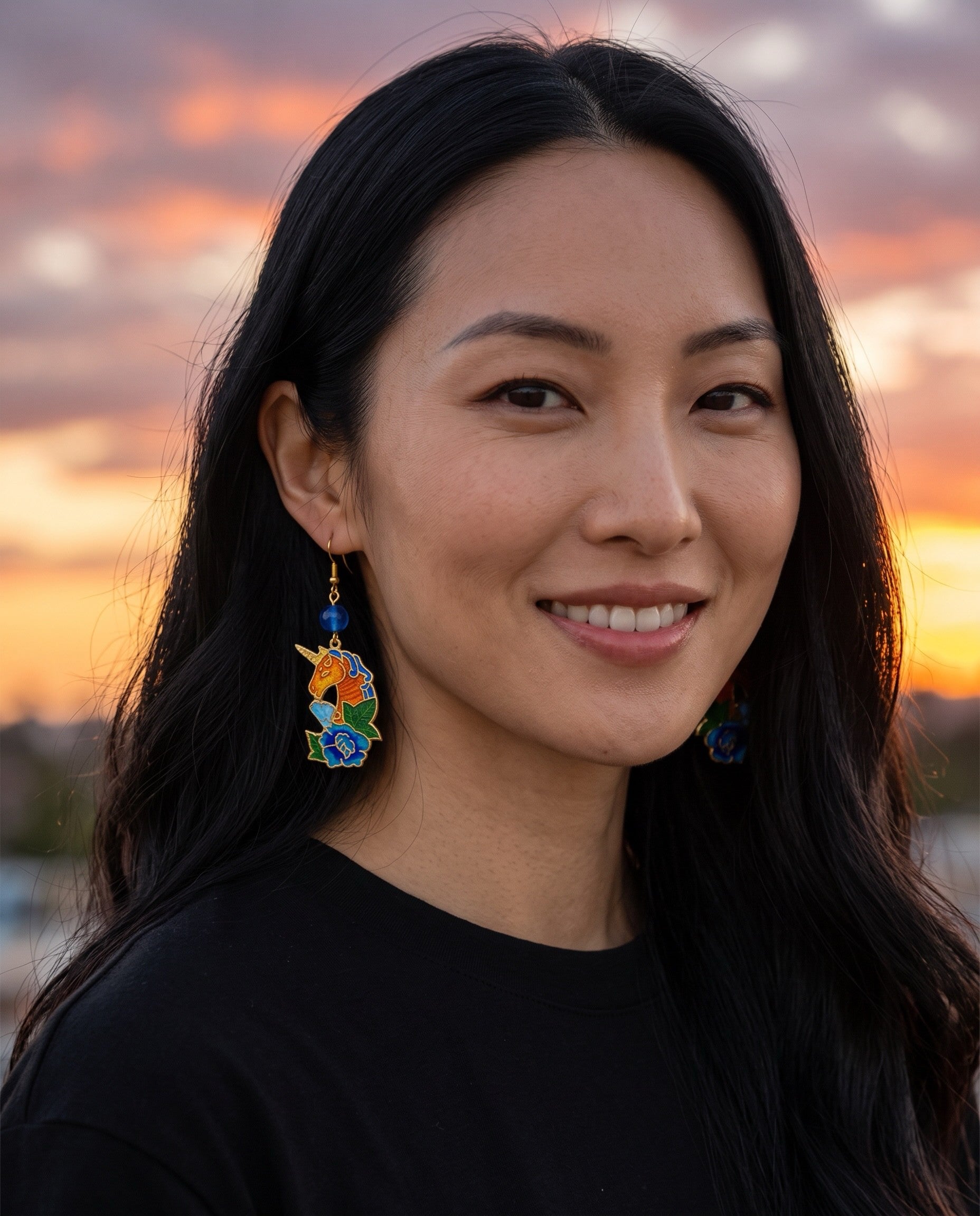 Heartfelt Creations unicorn dangle earrings with enamel floral details worn by a woman at sunset