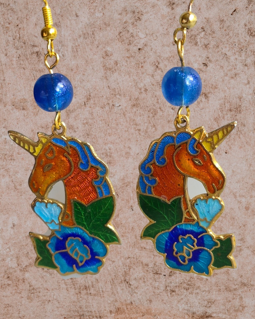 Heartfelt Creations unicorn dangle earrings with vibrant enamel floral details, gold-tone finish, and blue bead accents.