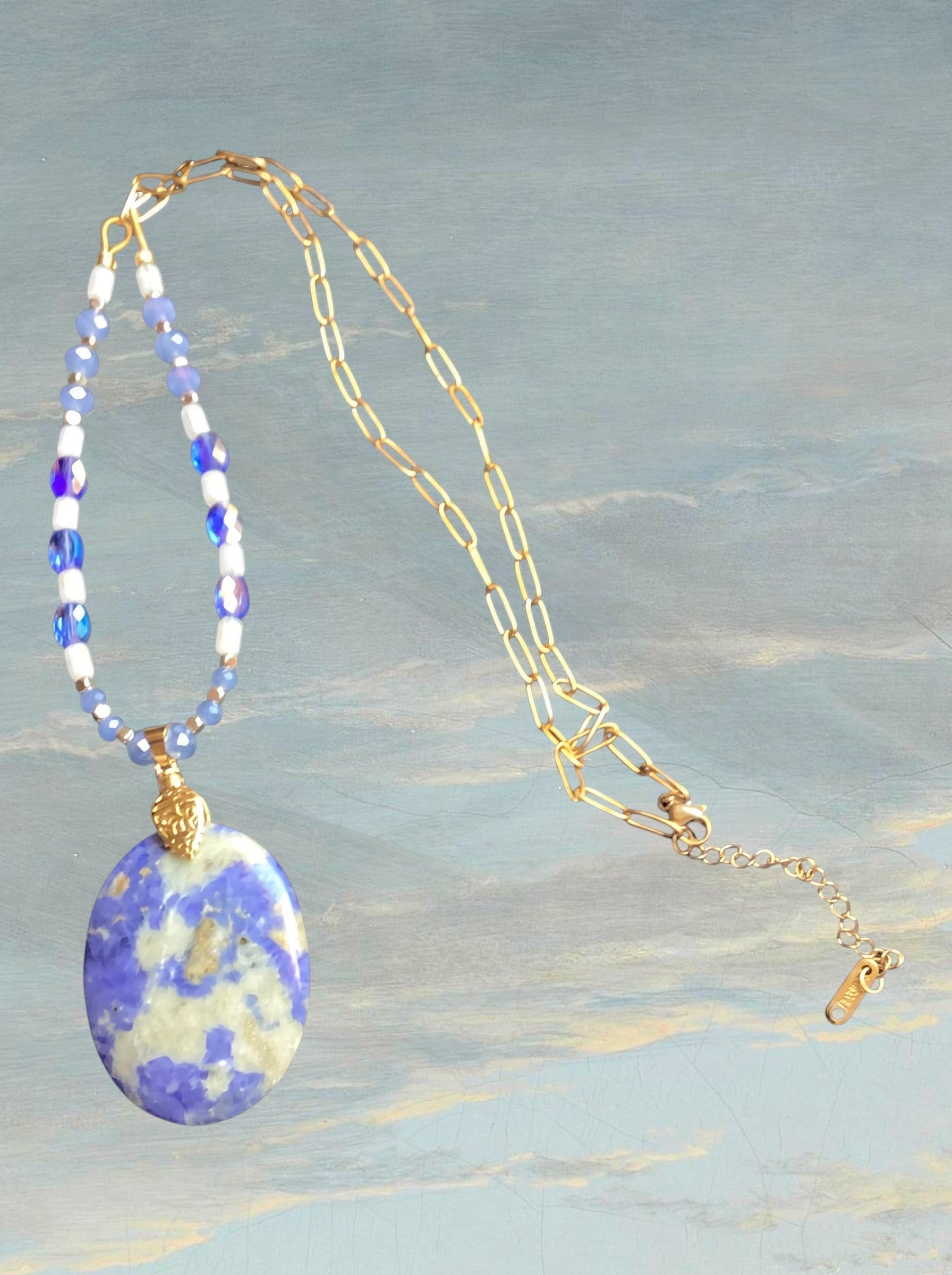 Heartfelt Creations necklace featuring a large violet and white stone pendant on a gold chain with blue faceted beads.