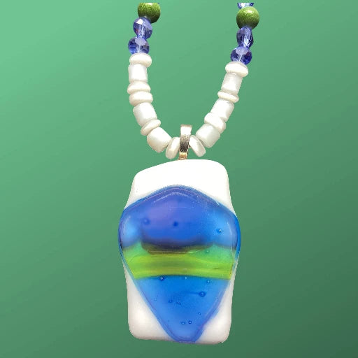 Heartfelt Creations' handmade jewelry set featuring a necklace and a multi-strand bracelet, both crafted with a mix of small, round, white, blue, and green beads, with the necklace featuring a prominent, rectangular, fused glass pendant with a vibrant blue, green, and white abstract design.