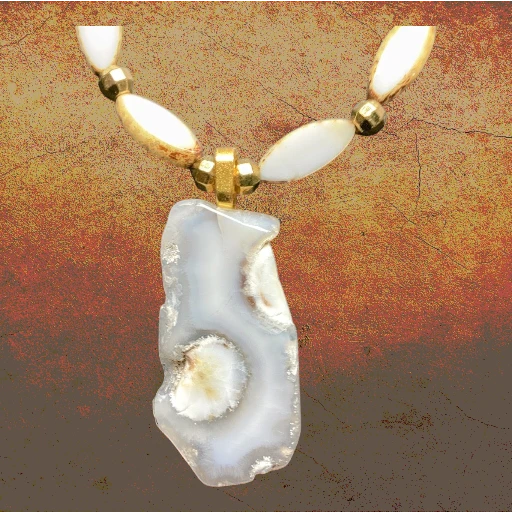 A beaded necklace with a large irregular agate stone pendant, featuring cream-colored beads and gold-toned spacers against a textured brown and gold background.