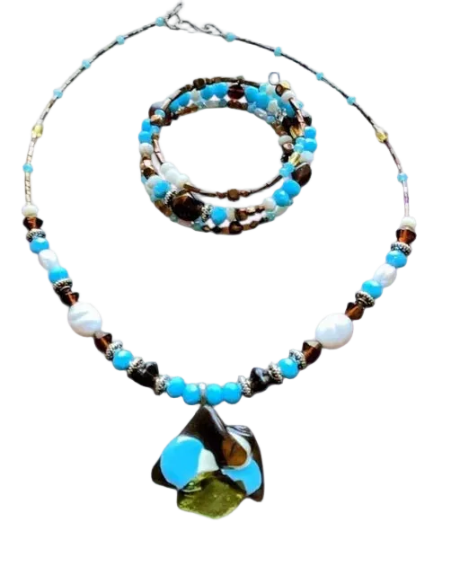 A beaded necklace with a large abstract glass pendant, displayed alongside a matching multi-strand beaded bracelet on a plain white background.