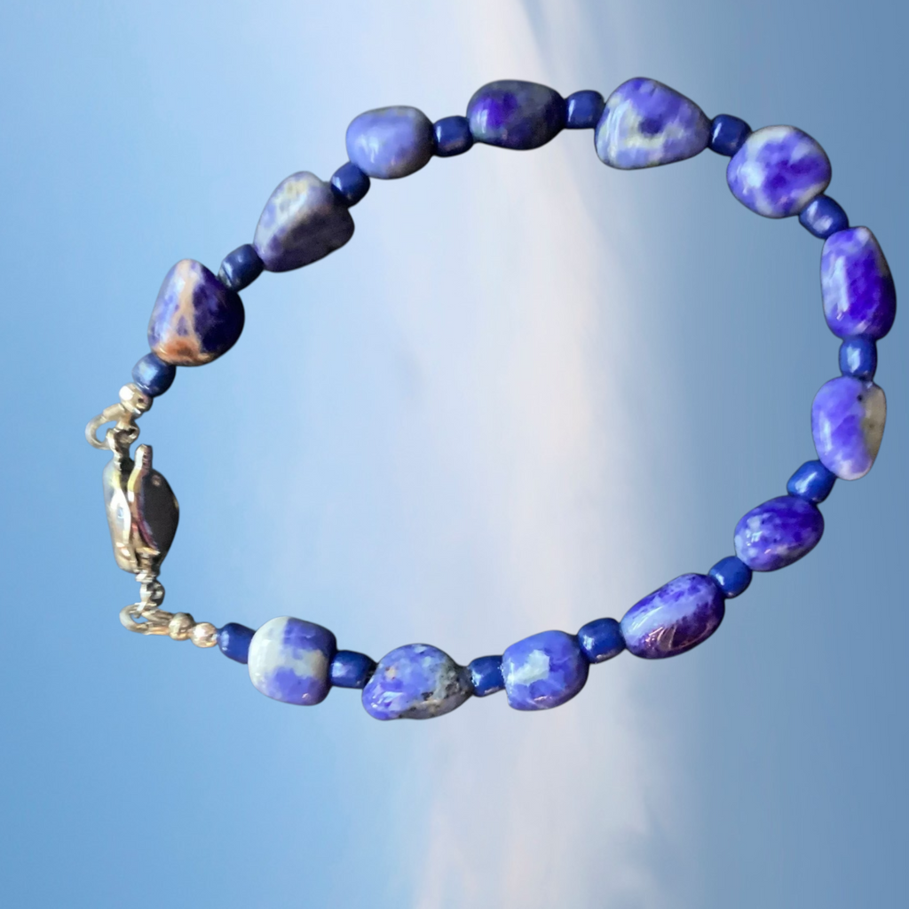 Blue beaded bracelet with a gold clasp against a blue sky background