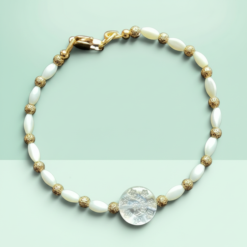 A beaded bracelet with white oval beads, textured gold spacer beads, a gold clasp, and a central round clear stone charm, displayed on a light mint green background.