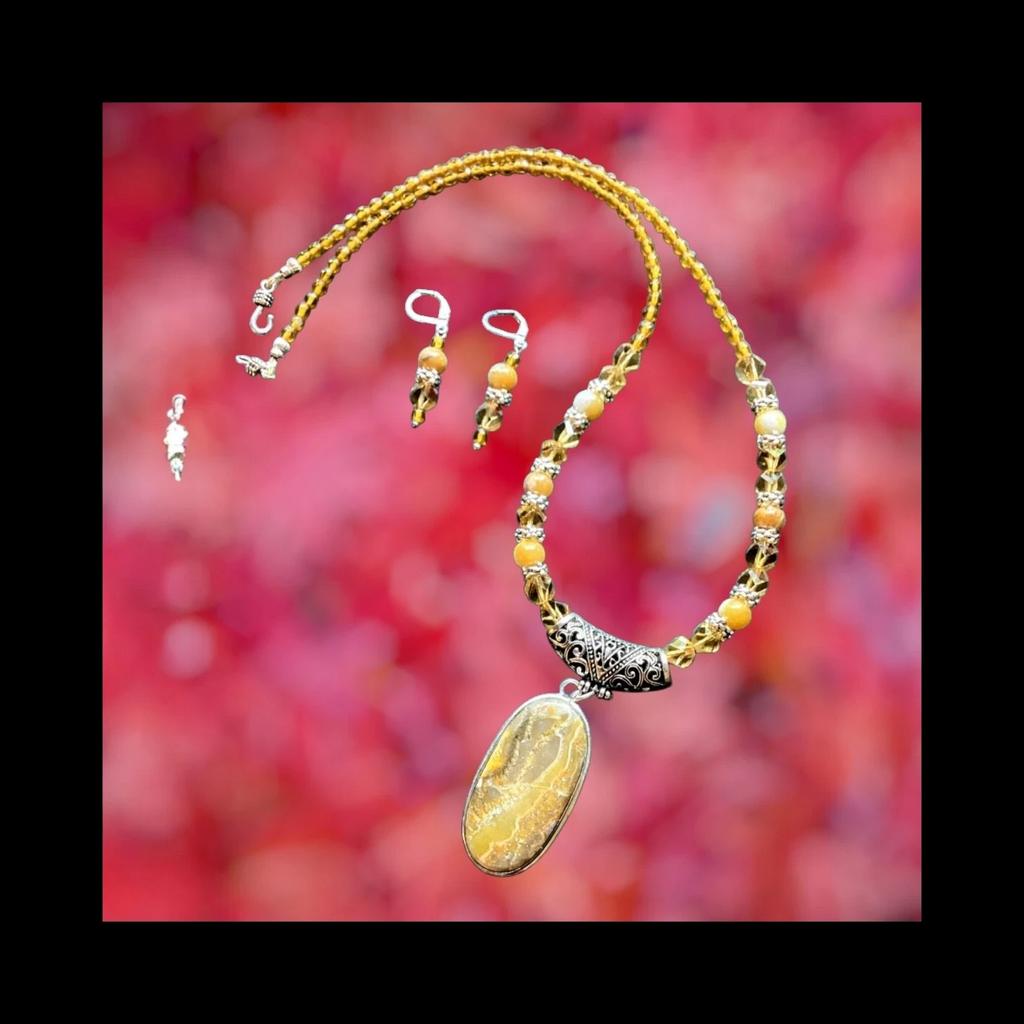 Heartfelt Creations' handcrafted jewelry set featuring a  Bumblebee Jasper and 925 silver plated pendant necklace and matching earrings.  The necklace is composed of small, faceted yellow and orange beads, a large oval-shaped, polished stone pendant with a yellow and white marbled pattern, and a decorative, ornate silver-toned metal clasp, and the earrings consisting of a single yellow bead and a smaller, matching orange bead on a silver-toned hook.