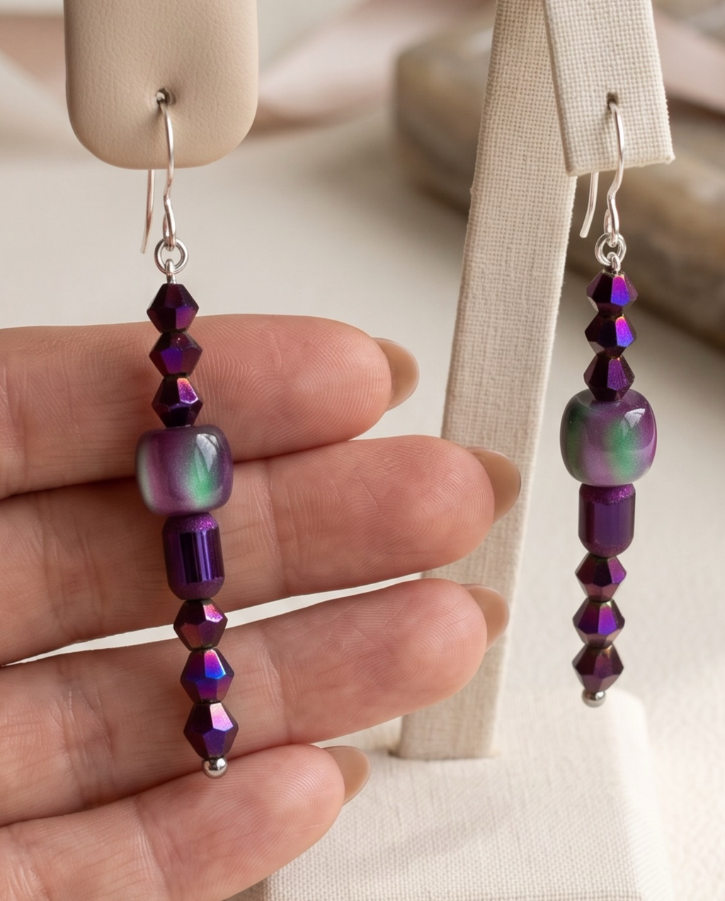 A pair of silver-toned dangle earrings with textured disc and bead details, a knotted rope-like drop, and polished ball ends, shown against a purple studio background.