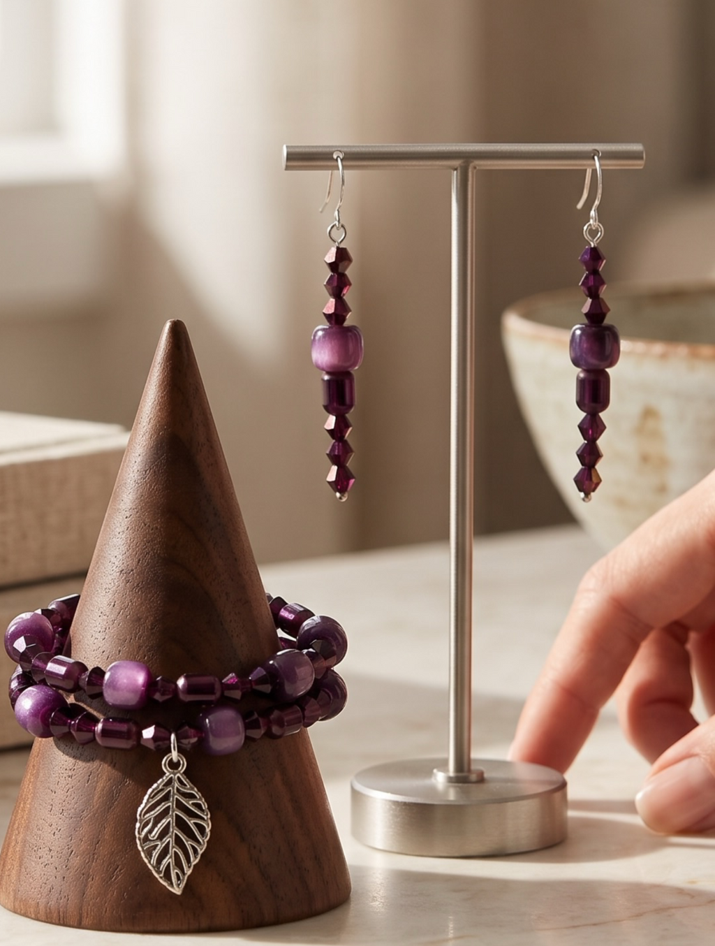 A pair of silver-toned dangle earrings displayed on a translucent white stand against a dark gray background. Each earring has a textured metallic gold disc, a faceted black stone, and a long silver chain ending in a polished bead.