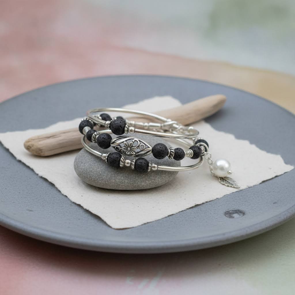 Heartfelt Creations' multiwrap specialty:  A bracelet with  two silver-toned bangle coils with black lava stone beads  and one silver-toned coil featuring a silver floral filigree charm, a silver leaf charm, and a white pearl bead.