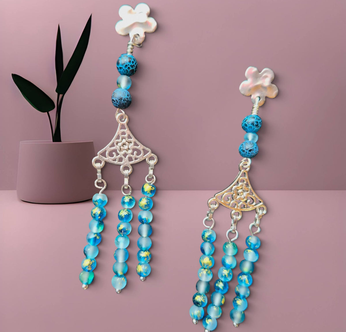 Pair of blue beaded earrings with floral and decorative elements on a pink background