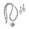 Heartfelt Creations  handmade jewelry set featuring a necklace and matching earrings, crafted from various black, white, and silver beads, with a circular, speckled granite-like stone pendant on the necklace and intricate, black filigree leaf-shaped pendants on the earrings.