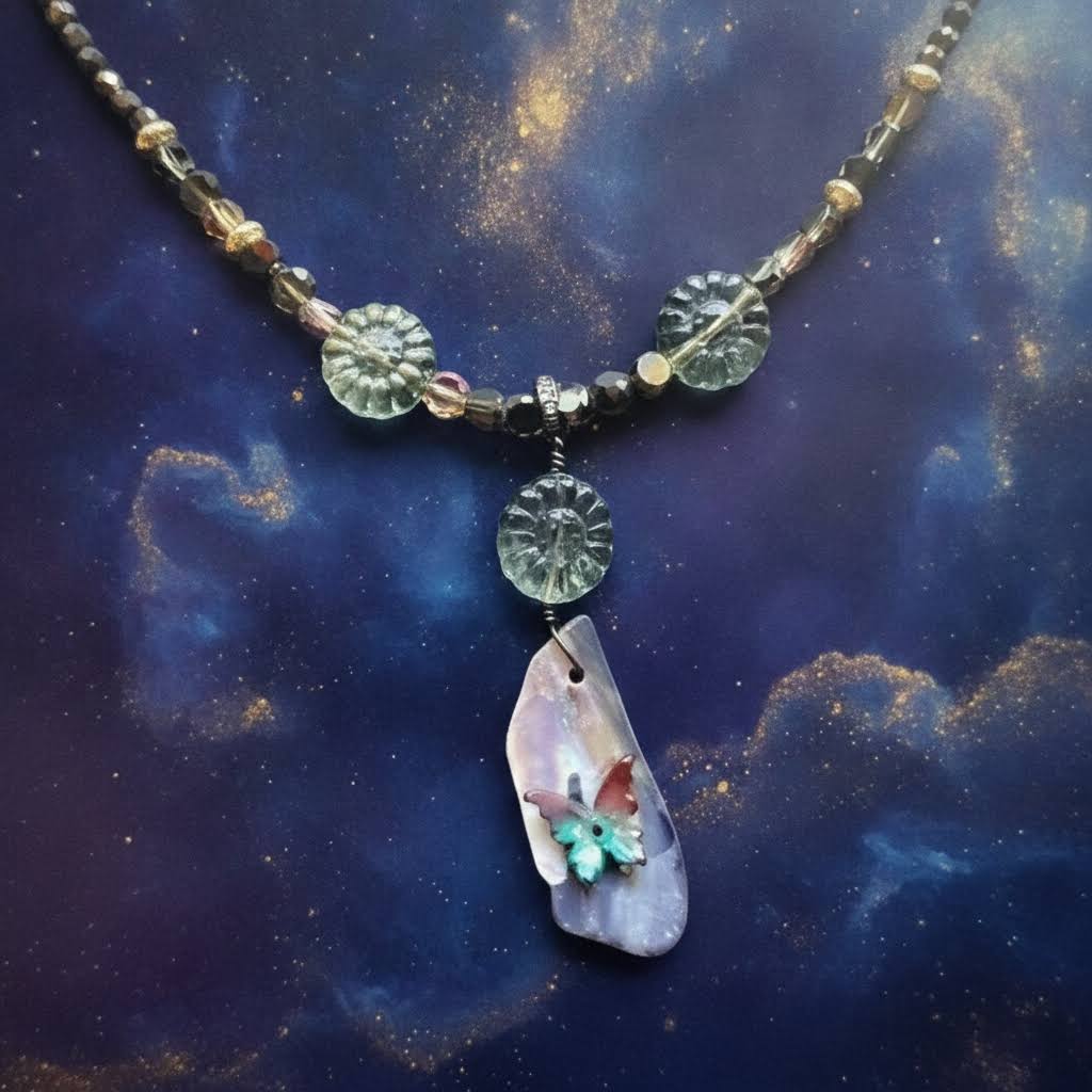 a handcrafted necklace and earring set featuring a delicate beaded chain of small, dark grey and golden beads, with a central pendant made of a polished, iridescent purple and white shell piece adorned with a small, colorful butterfly motif, accompanied by matching earrings with a single, translucent, light green floral-shaped bead