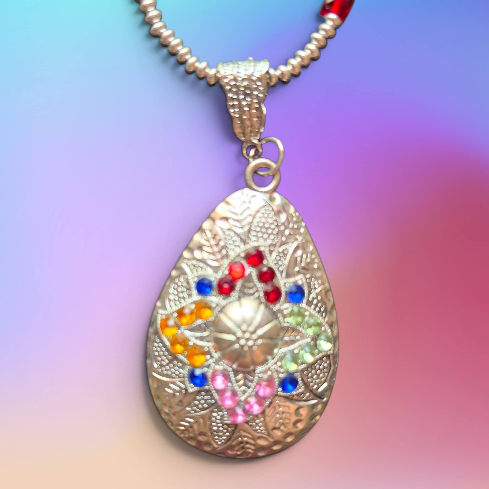a delicate, handmade necklace featuring a thin, silver-toned chain adorned with small, multi-colored glass beads, leading to a teardrop-shaped pendant with a mosaic-like pattern of tiny, vibrant stones.