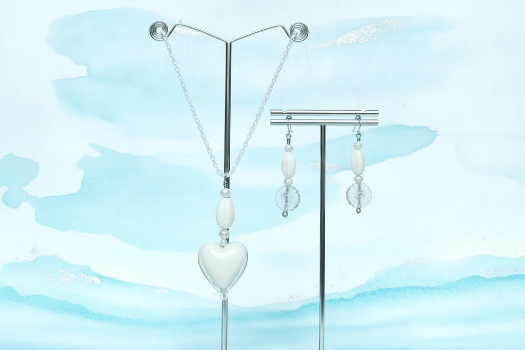 Heartfelt Creations offers a handcrafted  delicate jewelry set featuring a silver chain necklace with a heart-shaped, translucent white glass lampwork pendant and a pair of matching earrings with a combination of light white   and clear glass beads, with floral charms.