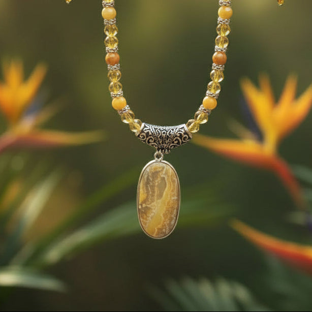 Heartfelt Creations' handcrafted jewelry set featuring a  Bumblebee Jasper and 925 silver plated pendant necklace and matching earrings.  The necklace is composed of small, faceted yellow and orange beads, a large oval-shaped, polished stone pendant with a yellow and white marbled pattern, and a decorative, ornate silver-toned metal clasp, and the earrings consisting of a single yellow bead and a smaller, matching orange bead on a silver-toned hook.