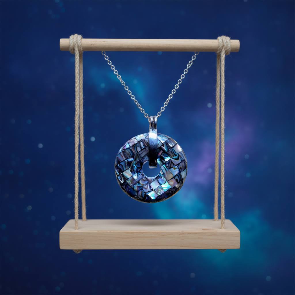 a circular, iridescent abalone shell pendant with a mosaic-like pattern, featuring a central circular cutout and a polished silver bail, suspended from a silver chain against a dark blue, starry sky background.