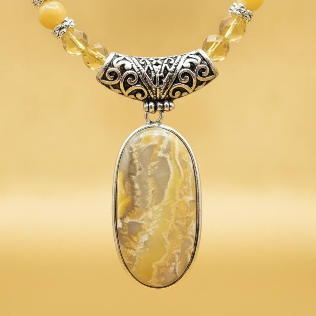 Heartfelt Creations' handcrafted jewelry set featuring a  Bumblebee Jasper and 925 silver plated pendant necklace and matching earrings.  The necklace is composed of small, faceted yellow and orange beads, a large oval-shaped, polished stone pendant with a yellow and white marbled pattern, and a decorative, ornate silver-toned metal clasp, and the earrings consisting of a single yellow bead and a smaller, matching orange bead on a silver-toned hook.