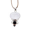 a handmade sterling silver pendant featuring a large, oval-shaped white moonstone cabochon and a smaller, teardrop-shaped faceted smoky quartz gemstone, connected by intricate silver wire scrollwork, suspended from a braided brown leather cord.