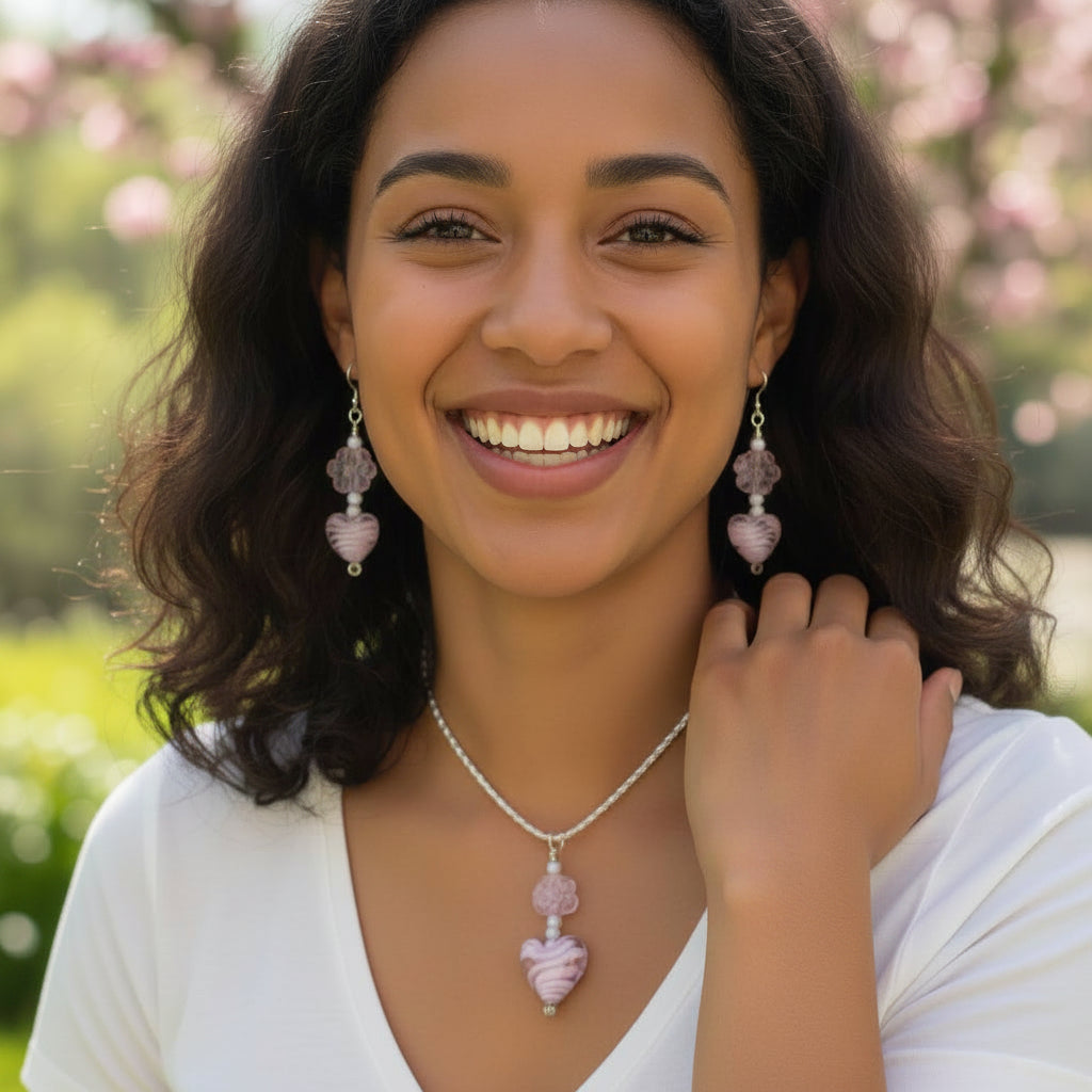 Heartfelt Creations offers a matching set of handcrafted jewelry, including a necklace and a pair of earrings, featuring silver-toned chains and hooks, with each piece adorned with a pale pink, swirled lampwork  glass heart bead and a delicate, clear glass flower bead.