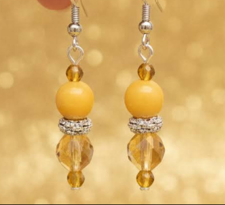 Heartfelt Creations' handcrafted jewelry set featuring a  Bumblebee Jasper and 925 silver plated pendant necklace and matching earrings.  The necklace is composed of small, faceted yellow and orange beads, a large oval-shaped, polished stone pendant with a yellow and white marbled pattern, and a decorative, ornate silver-toned metal clasp, and the earrings consisting of a single yellow bead and a smaller, matching orange bead on a silver-toned hook.