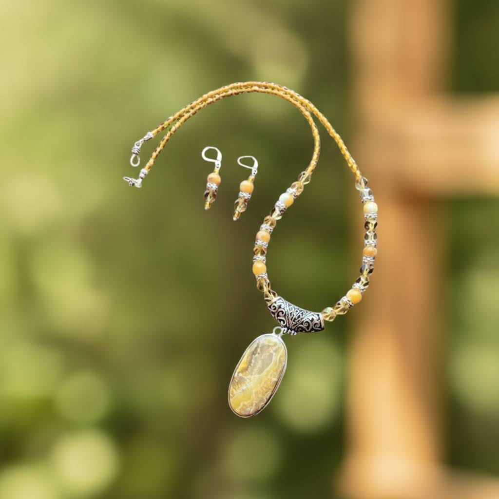 Heartfelt Creations' handcrafted jewelry set featuring a  Bumblebee Jasper and 925 silver plated pendant necklace and matching earrings.  The necklace is composed of small, faceted yellow and orange beads, a large oval-shaped, polished stone pendant with a yellow and white marbled pattern, and a decorative, ornate silver-toned metal clasp, and the earrings consisting of a single yellow bead and a smaller, matching orange bead on a silver-toned hook.
