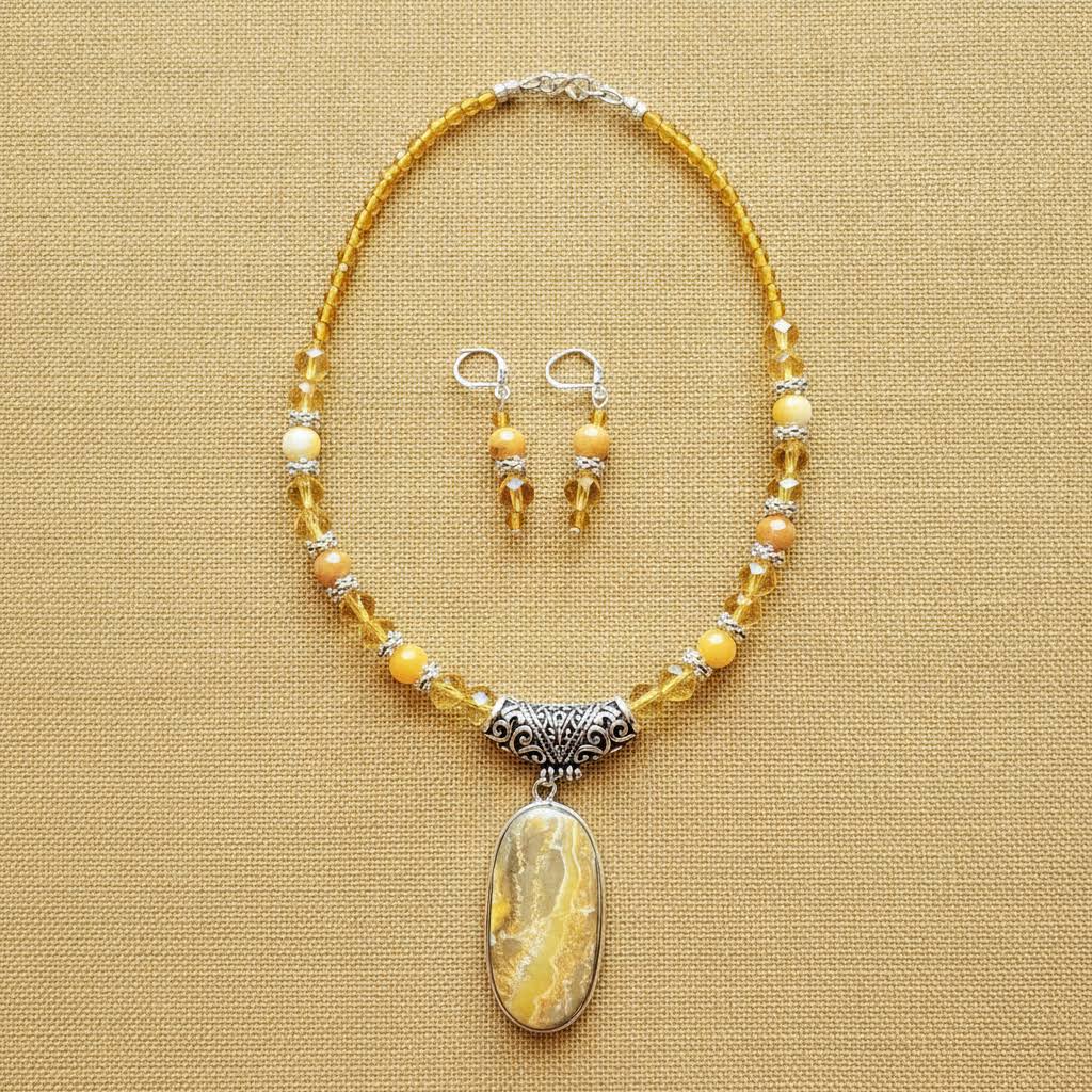 Heartfelt Creations' handcrafted jewelry set featuring a  Bumblebee Jasper and 925 silver plated pendant necklace and matching earrings.  The necklace is composed of small, faceted yellow and orange beads, a large oval-shaped, polished stone pendant with a yellow and white marbled pattern, and a decorative, ornate silver-toned metal clasp, and the earrings consisting of a single yellow bead and a smaller, matching orange bead on a silver-toned hook.