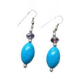 A pair of dangle earrings featuring textured turquoise blue oval beads, a small faceted purple crystal, and silver-tone metal hooks and spacer beads, shown against a plain white background.