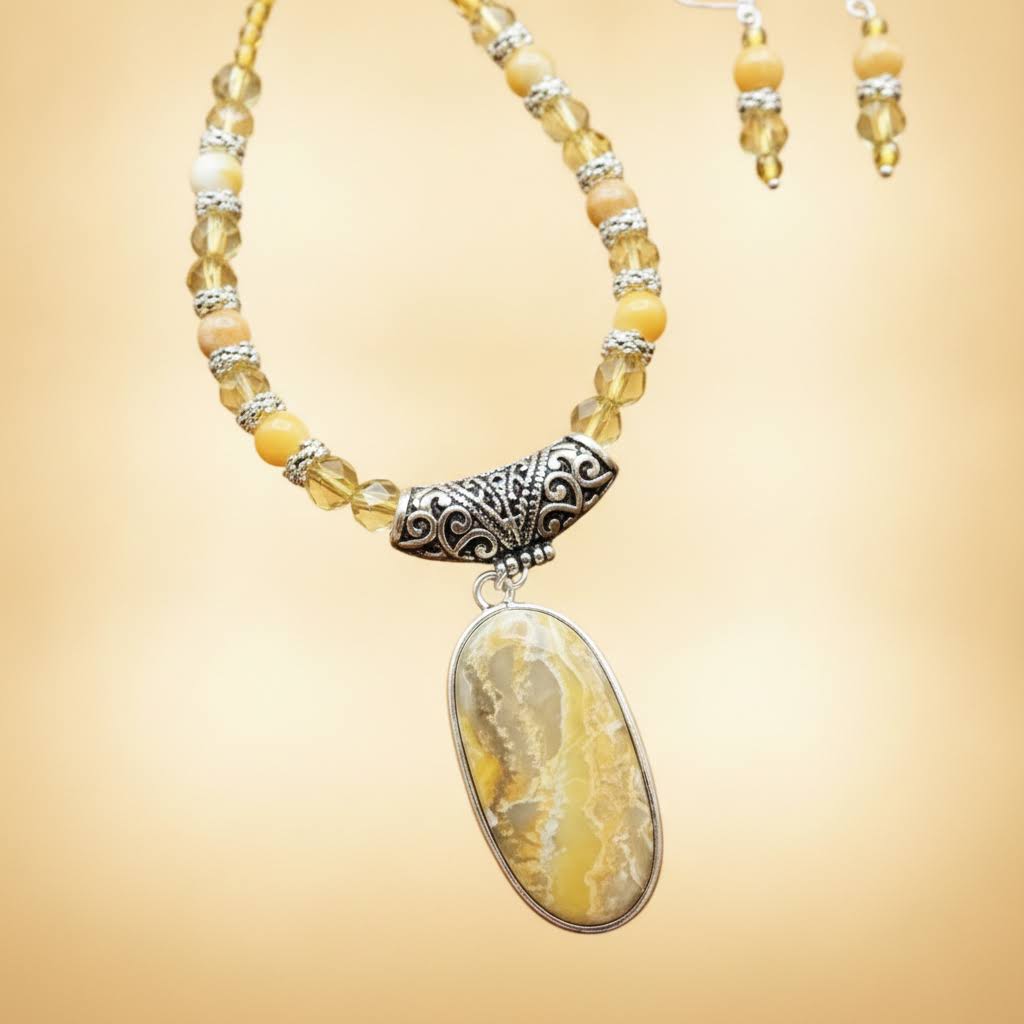Heartfelt Creations' handcrafted jewelry set featuring a  Bumblebee Jasper and 925 silver plated pendant necklace and matching earrings.  The necklace is composed of small, faceted yellow and orange beads, a large oval-shaped, polished stone pendant with a yellow and white marbled pattern, and a decorative, ornate silver-toned metal clasp, and the earrings consisting of a single yellow bead and a smaller, matching orange bead on a silver-toned hook.