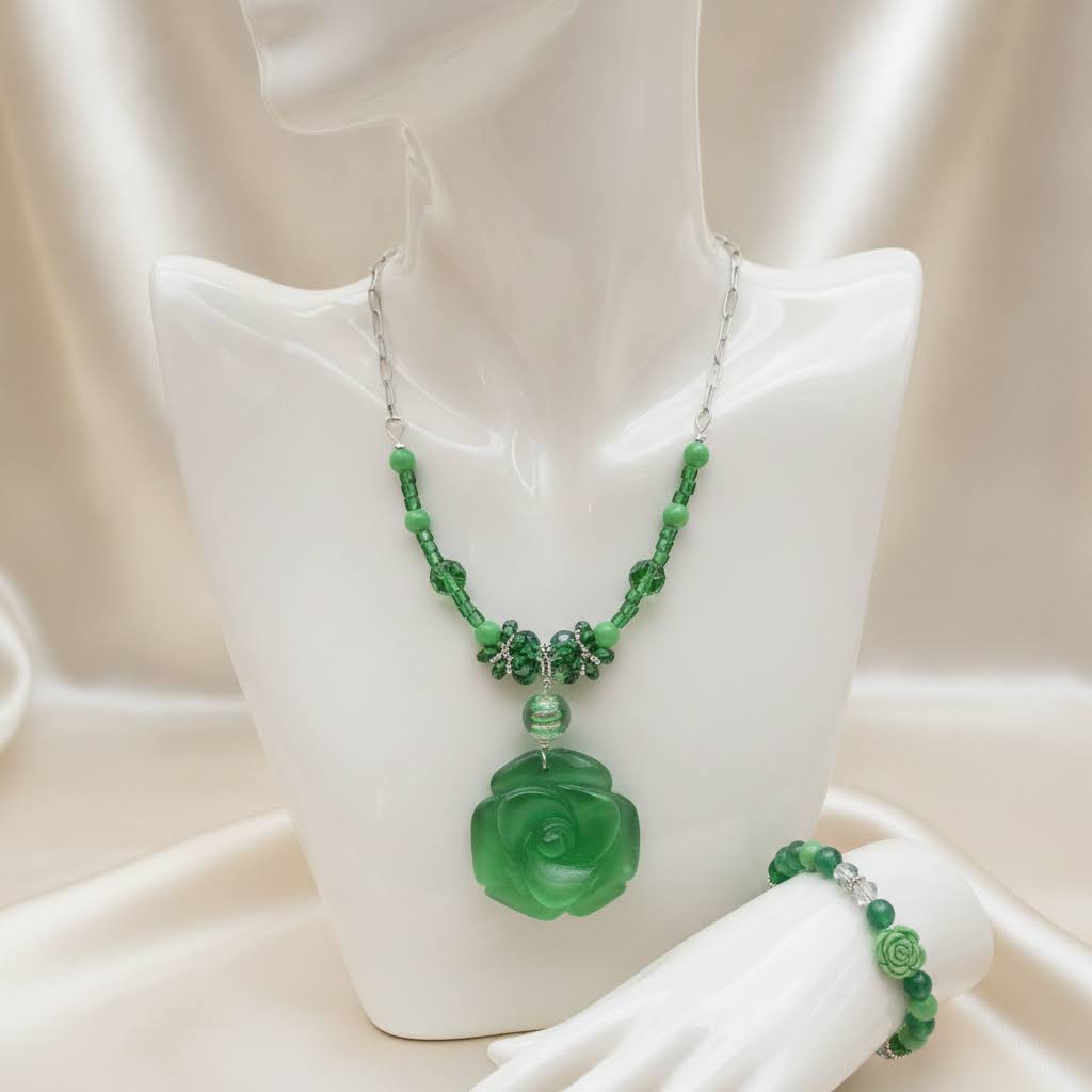 Heartfelt Creations' offers this stunning, nature-inspired beaded necklace and bracelet set. Featuring a vibrant palette of lush greens, this set is designed to add a touch of botanical elegance to any outfit. The centerpiece of the necklace is a beautifully detailed, frosted glass floral charm that captures the essence of a blooming rose, complemented by a variety of green beads that offer a rich, multi-textured look. The matching bracelet echoes this design, creating a cohesive and polished aesthetic.