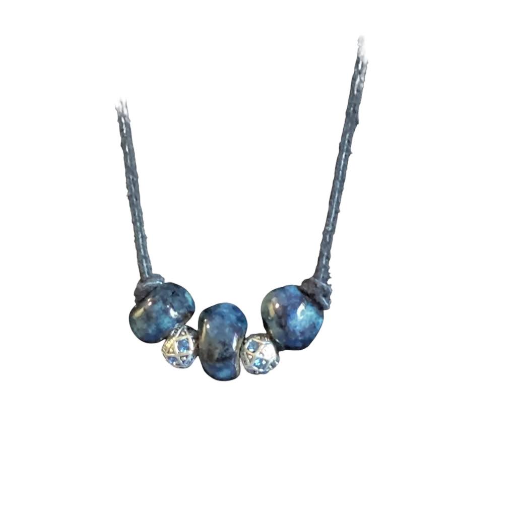 Heartfelt Creations'  handmade necklace featuring three large, glossy, deep blue home-made ceramic beads with a mottled texture, separated by two ornate, silver-toned metal spacer beads with a star-like pattern and small blue crystal accents, all strung on a dark cord.