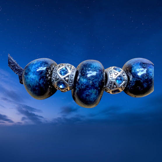 Heartfelt Creations'  handmade necklace featuring three large, glossy, deep blue home-made ceramic beads with a mottled texture, separated by two ornate, silver-toned metal spacer beads with a star-like pattern and small blue crystal accents, all strung on a dark cord.