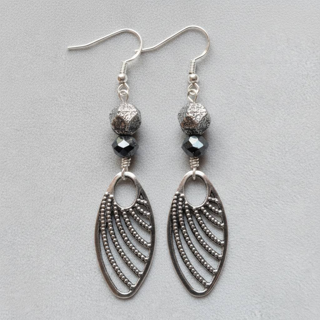 Heartfelt Creations  handmade jewelry set featuring a necklace and matching earrings, crafted from various black, white, and silver beads, with a circular, speckled granite-like stone pendant on the necklace and intricate, black filigree leaf-shaped pendants on the earrings.