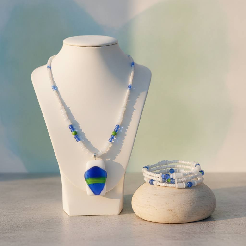 Heartfelt Creations' handmade jewelry set featuring a necklace and a multi-strand bracelet, both crafted with a mix of small, round, white, blue, and green beads, with the necklace featuring a prominent, rectangular, fused glass pendant with a vibrant blue, green, and white abstract design.