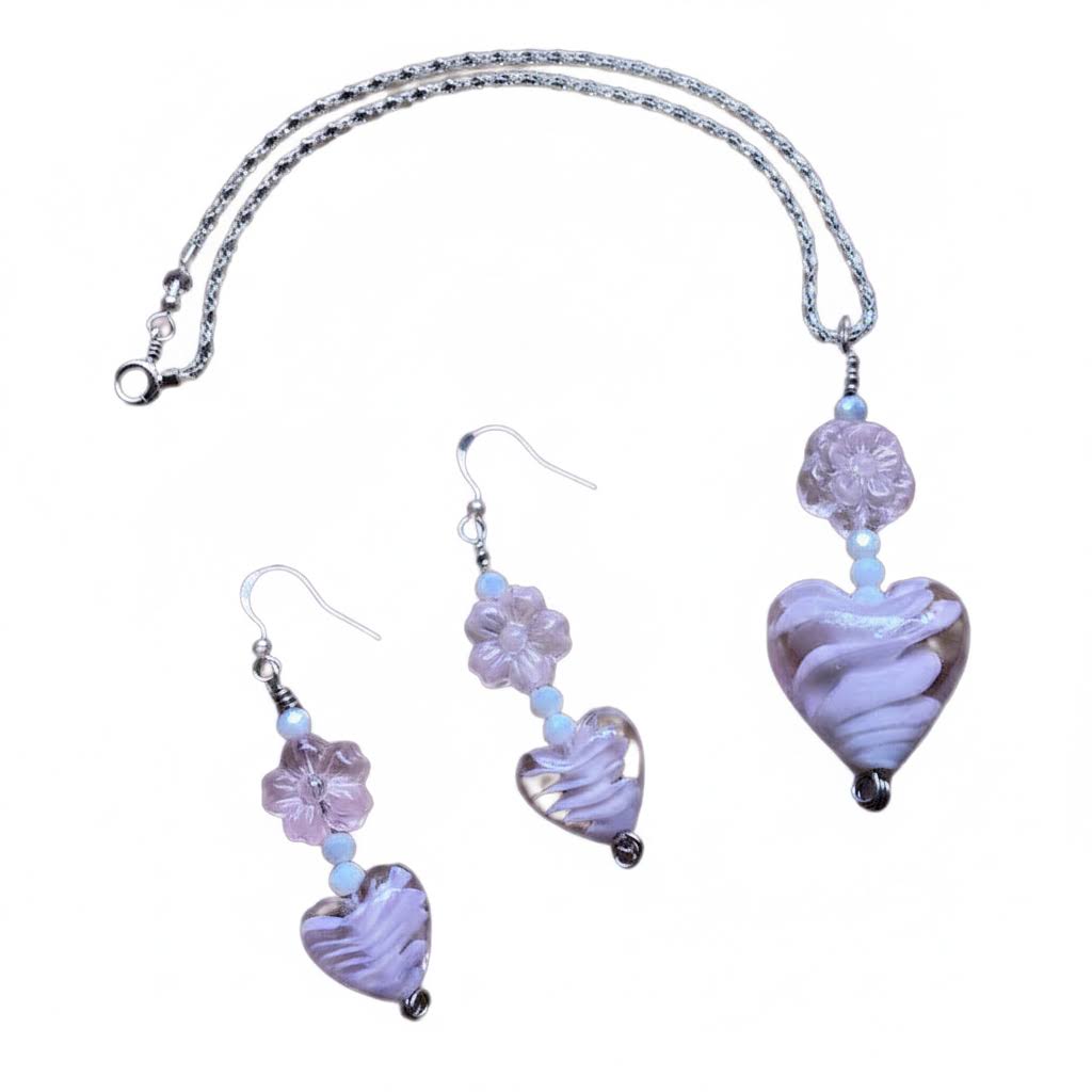 Heartfelt Creations offers a matching set of handcrafted jewelry, including a necklace and a pair of earrings, featuring silver-toned chains and hooks, with each piece adorned with a pale pink, swirled lampwork  glass heart bead and a delicate, clear glass flower bead.