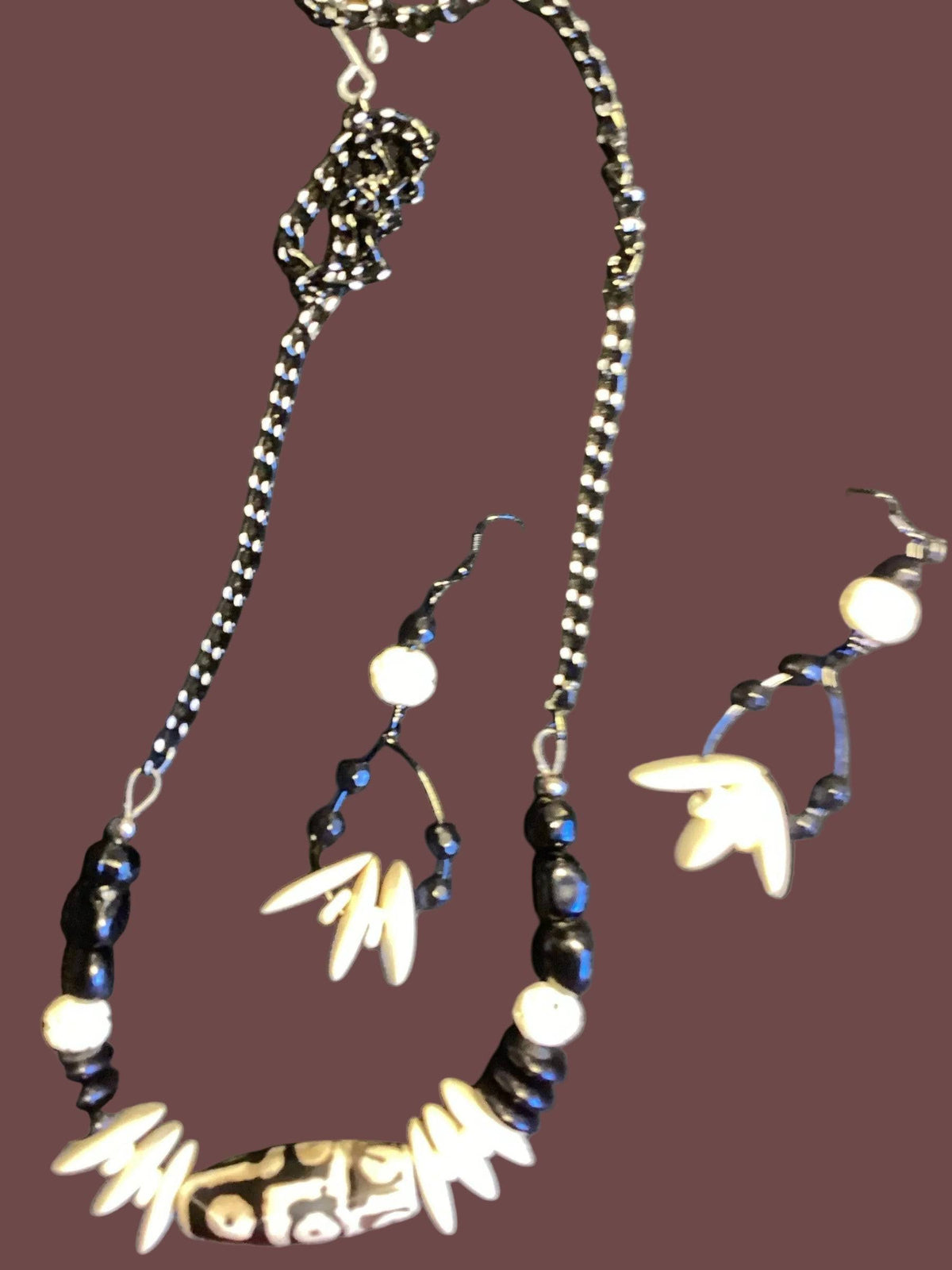 Heartfelt Creations offers a uniquely designed  jewelry set featuring a necklace, matching earrings, and a bracelet. The necklace includes black stones, white ivory-like beads, and a central black/white/grey marbled focal bead on the necklace.  A gun metal chain completes the necklace.  Finally, a simple yet striking bracelet with carved beads and drop earrings offering all the features, completes the set,