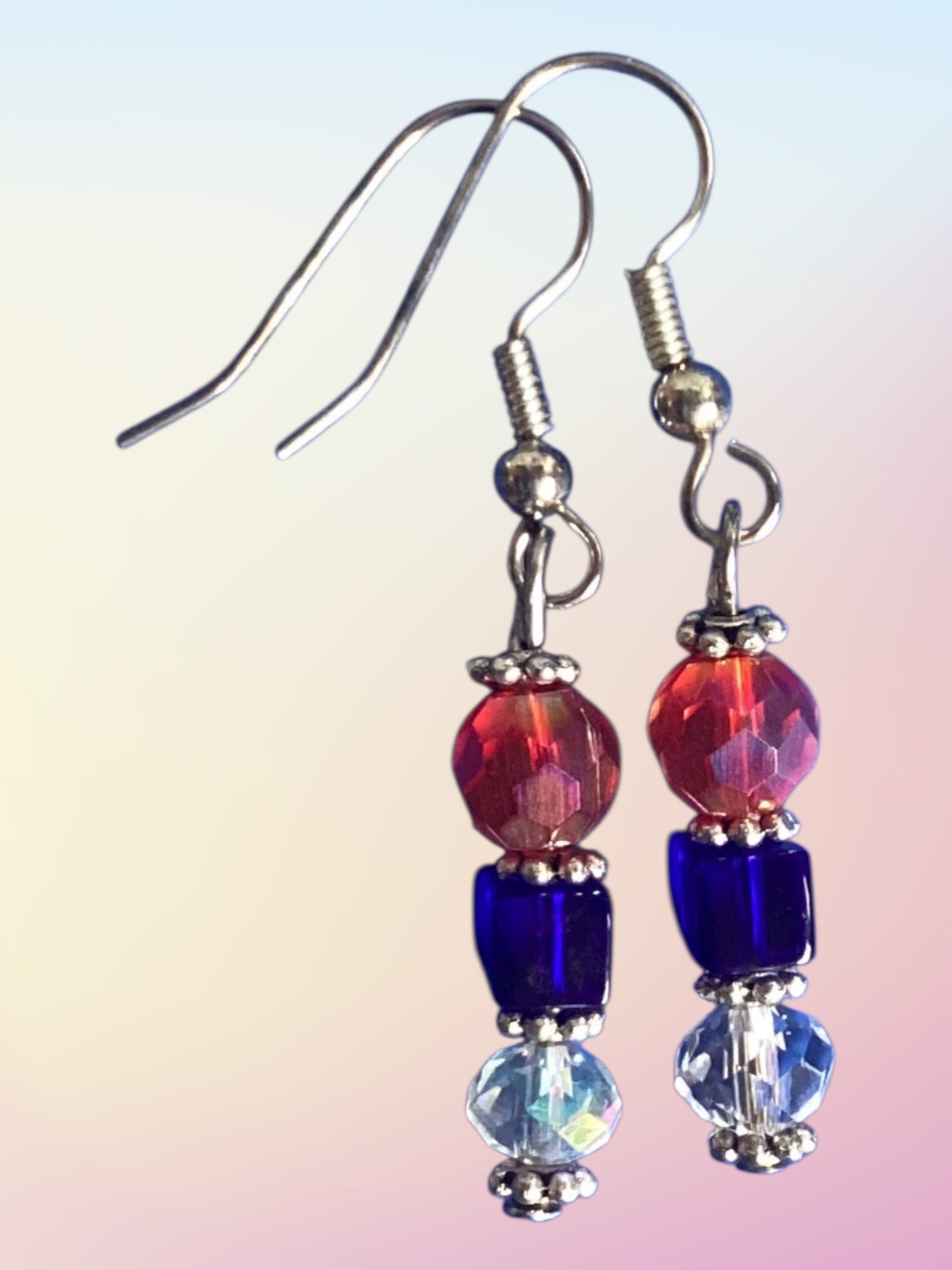 Beaded earrings with red, blue, and clear beads on a gradient background